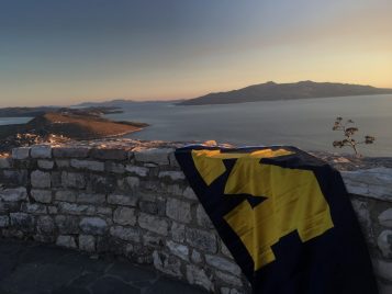 At dusk, there is a low wall built from rocks. There are distant islands in a body of water and a large sky that shows pink on the horizon.